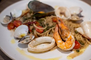 Karides, kalamar, midye ve istiridye ile servis edilen deniz ürünleri makarnası tabağında spagetti, kiraz domatesleri ve sos içinde yeşil bezelye ile karıştırılmış.