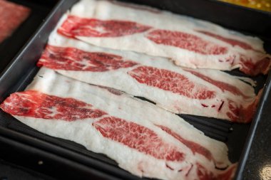 Yakın plan kesilmiş çiğ et, bir tabakta, sıcak bir tencerede pişirilmeye hazır.