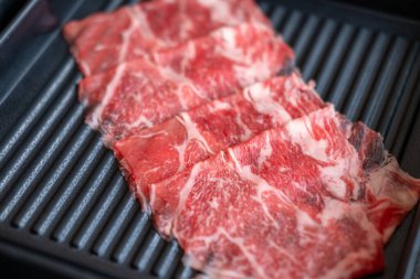 Yakın plan kesilmiş çiğ et, bir tabakta, sıcak bir tencerede pişirilmeye hazır.