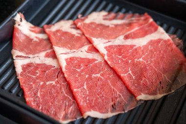 Yakın plan kesilmiş çiğ et, bir tabakta, sıcak bir tencerede pişirilmeye hazır.