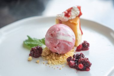 Peynirli kek, parçalanmış bisküvi, çırpılmış krema ve taze böğürtlen ile servis edilen çilekli dondurma.