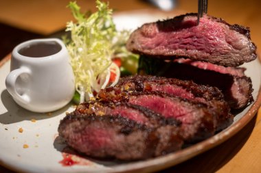 Tabakta sos ve sebzeyle servis edilen orta pişmiş wagyu eti üzerine bir çatal.