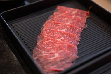 Yakın plan kesilmiş çiğ et, bir tabakta, sıcak bir tencerede pişirilmeye hazır.