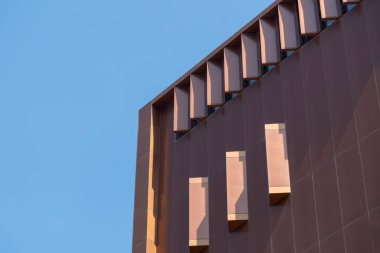 Dikey ve çapraz metal yüzgeçler ve cam pencerelerden oluşan geometrik desenli modern bir bina cephesi