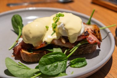 Benedict yumurtaları tabakta servis ediliyor. Domuz pastırması, haşlanmış yumurta ve Hollandaise sosuyla kaplanmış iki yarım tosttan oluşan yaygın bir Amerikan kahvaltısıdır..
