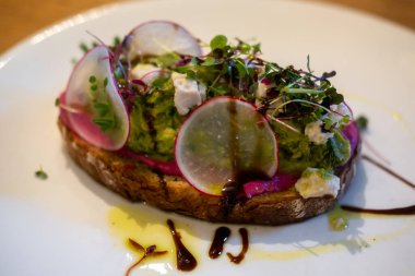 Tabakta, ahşap masada servis edilen soslu avokado tostu.