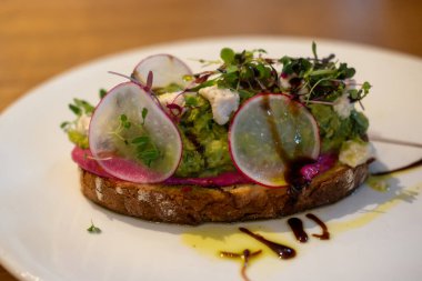 Tabakta, ahşap masada servis edilen soslu avokado tostu.