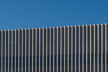 Güçlü gölge desenli dikey metal yüzgeçli modern bina cephesi açık mavi gökyüzüne karşı kurulur..