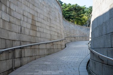 Çelik tırabzanlarla kaplı eğri taş bir yol, açık mavi gökyüzünün altında yokuş yukarı ve yeşilliklerle çevrili..
