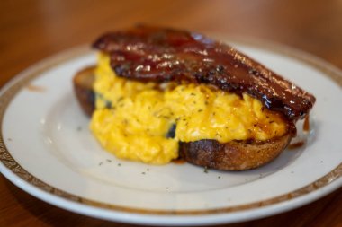 Çırpılmış yumurta ve kalın pastırmalı tost, tabakta servis edilir.
