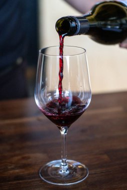 Bir adam bardağa kırmızı şarap döküyor.