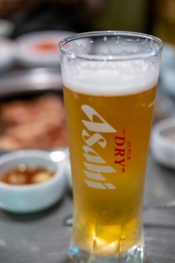 Seul, Güney Kore - 16 Haziran 2025: Arkasında Kore usulü barbekü olan yarım litre Asahi. Japon pilav birası, arpa arpası ve Japonya 'nın en büyük dört bira imalatçısı..