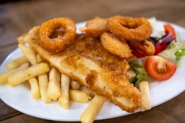 Tabakta servis edilen kızarmış soğan halkalı balık ve patates kızartması salatası.