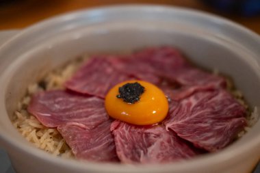 Kavanozda sığır yağında pilav, üstünde dilimlenmiş et ve yumurta sarısı.