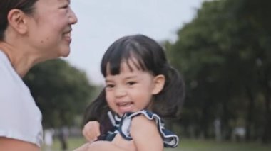 Genç Asyalı anne tatlı kızını kucağına alır, havada yükselir ve gülümseyerek etrafında döner. Anne çocuk ilişkiyi sever ya da mutlu çocuk konseptini, yavaş çekim sevimli aile anını