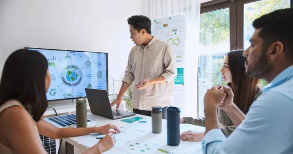 アジアの男性は モニター上のEsgトピックプレゼンテーションのためのラップトップコンピュータを使用して チームミーティングで多民族ビジネスマンの若いグループをリードします 持続可能なビジネスプラクティス 人々は家庭のコンセプトで働く ストック画像