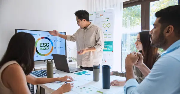 アジアの男性は モニター上のEsgトピックプレゼンテーションのためのラップトップコンピュータを使用して チームミーティングで多民族ビジネスマンの若いグループをリードします 持続可能なビジネスプラクティス 人々は家庭のコンセプトで働く ストックフォト