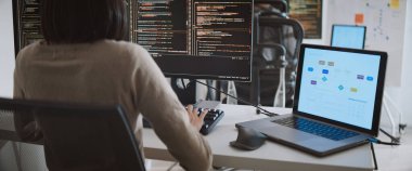 Genç yetişkin Asyalı erkek, kadın yazılım geliştirici masaüstü bilgisayarında kodlama programı. Erkek, kadın evden çalışıyor, uzaktan çalışıyor, serbest programcılık yapıyor, akıllı dijital göçebe yaşam tarzı kavramı.