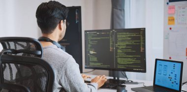 Genç yetişkin Asyalı erkek yazılım geliştirici kodlama programı masaüstü bilgisayarında. Evden çalışan, uzaktan çalışan, serbest çalışan programcı işi, akıllı dijital göçebe yaşam tarzı konsepti