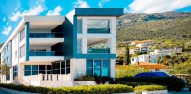 Dairelerin modern evi bir dağ sırasının arka planına karşı. Mavi gökyüzü güneşli. Minimalist ve doğrusal mimari. Yaz boyunca yeşil tepelerin arka planında panoramik manzara.