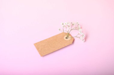 Kahverengi etiketteki beyaz çiçeklerin zarif bir düzeni pembe bir arkaplana karşı duruyor..