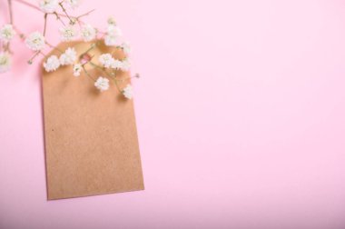 Boş bir kahverengi etiket yumuşak pembe arka planda narin beyaz çiçeklerin yanına yerleştirilir..