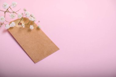 Kahverengi bir etiket pembe bir arka planda duruyor, narin beyaz çiçekli, basit bir sahne oluşturuyor..