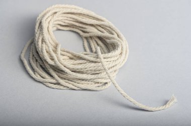 Sarmalanmış pamuk halat, doğal dokusunu ve görünümünü vurgulayarak pürüzsüz gri bir yüzeye dayanır..