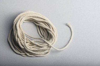 Sarmalanmış beyaz bir halat pürüzsüz gri bir yüzeye dayanır ve çarpık dokusunu ve uzunluğunu gösterir..