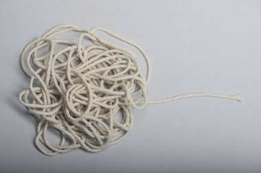 Beyaz bir ip uzunluğu, nötr bir yüzeye uzanan karmaşık bir düğüme dolanmış..