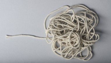 Kalın, dolambaçlı beyaz bir ip gri bir yüzeyde duruyor, çok yönlü doğasını sergiliyor..