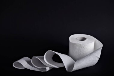 Bir rulo yumuşak beyaz tuvalet kağıdı koyu bir arka planda gevşiyor, banyo hijyenini vurguluyor..