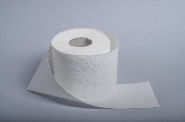 Bir rulo yumuşak, beyaz tuvalet kağıdı gri bir zemine karşı sergileniyor, temizliği sembolize ediyor.