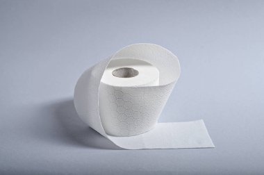 Bir rulo yumuşak, beyaz tuvalet kağıdı gri bir yüzeye oturmuş, dokusunu vurguluyor..