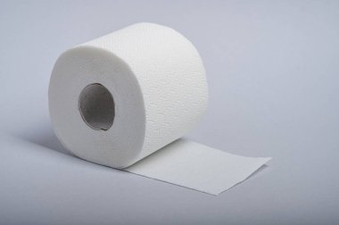 Bir rulo beyaz tuvalet kağıdı pürüzsüz gri bir yüzeye oturur ve hijyen önemini vurgular..