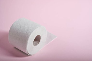 Yumuşak, beyaz tuvalet kağıdı pastel pembe arka planda yuvarlanıyor. Banyo hijyeni için ideal..