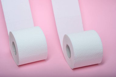 Pembe yüzeyde iki rulo yumuşak, beyaz tuvalet kağıdı..