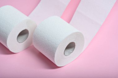 İki rulo yumuşak, beyaz tuvalet kağıdı pembe bir zemine oturup hijyen ve konforu vurguluyor..