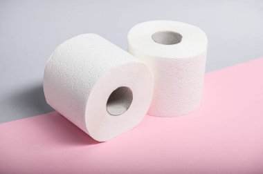 Pastel arka planda iki tane yumuşak beyaz tuvalet kağıdı rulosu banyo hijyeninin esaslarını ön plana çıkarıyor..