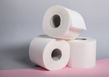 Üç rulo yumuşak beyaz tuvalet kağıdı istiflenmiş, pürüzsüz dokuları ve hijyenleri vurgulanıyor..