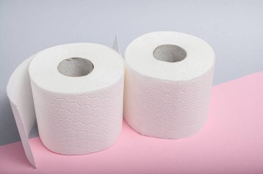 İki rulo yumuşak beyaz tuvalet kağıdı pembe bir tezgahın üzerinde, banyoda kullanılmaya hazır..