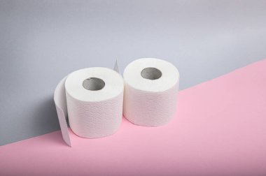 İki rulo yumuşak beyaz tuvalet kağıdı pembe arka planda oturuyor, temizliği vurguluyor..