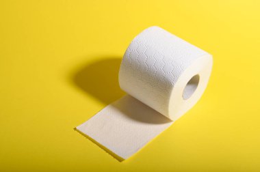 Bir rulo yumuşak tuvalet kağıdı yan yatar, sarı bir zeminde kısmen açılmış bir çarşaf..