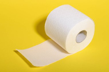 Bir rulo yumuşak beyaz tuvalet kağıdı parlak sarı bir zemin ile tezat oluşturur, hijyeni vurgular..