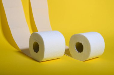 İki rulo yumuşak beyaz tuvalet kağıdı, parlak sarı bir zemine hafifçe açılır..