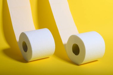 İki rulo yumuşak beyaz tuvalet kağıdı parlak sarı bir yüzeye oturur ve hijyene önem verir..