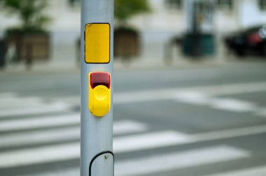 Açık gökyüzünün altındaki kalabalık bir şehir ortamında yaya geçidinin yanındaki bir direğe yerleştirilmiş yaya sinyal düğmesi.