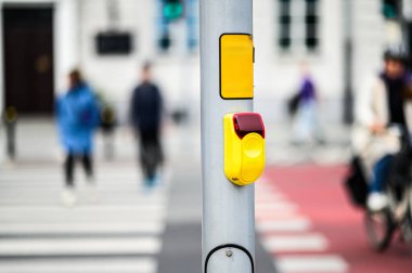 Bir trafik ışığı düğmesi ve yaya geçidi için bulanık yaya figürleri ve yoldan geçen bir bisikletçi.