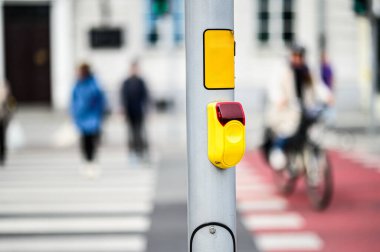 Bir trafik ışığı düğmesi ve yaya geçidi için bulanık yaya figürleri ve yoldan geçen bir bisikletçi.