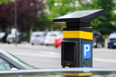 Parlak bir günde, park halindeki arabalar ve yeşilliklerle çevrili modern bir park kulübesi şehirde belirgin bir şekilde yer alır..